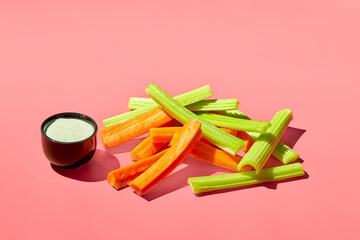 Raw carrot pieces and celery stalks with sauce on color background
