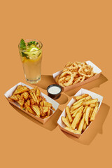 French fries of two kinds and fried onion rings in breadcrumbs with sauce and lemonade on an orange background