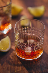 Glasses of whiskey with ice and lemon slices on a wooden table in the rays of light. Shallow depth of field