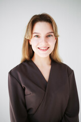 Smiling woman in brown medical scrubs posing on white background, close-up studio portrait.  
