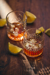 Glasses of whiskey with ice and lemon slices on a wooden table in the rays of light. Shallow depth of field