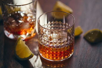 Glasses of whiskey with ice and lemon slices on a wooden table in the rays of light. Shallow depth of field
