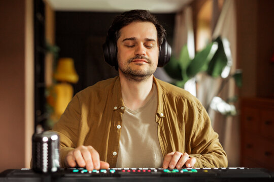 Man playing synthesizer at home with headphones