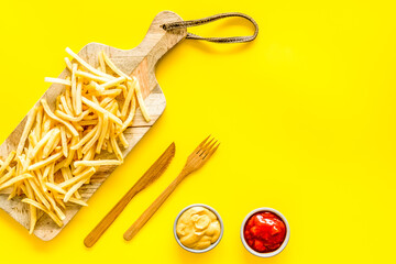 French fries served on cutting board on yellow table top-down copy space