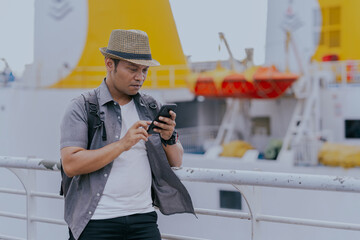 Tourist asian man backpacker enjoying solo travel vacation using cell phone on the ship. Tourism...