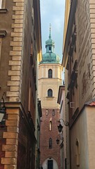 Historic church tower with a green dome seen through a narrow old town alley, framed by charming decorative buildings