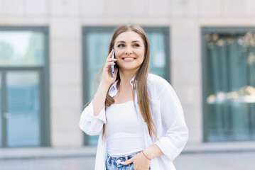 Attractive young woman in casual clothing talking on her mobile phone while walking outdoors in the city. Freelance, business, work, communication