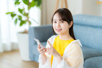 部屋でスマホを操作する若い女性