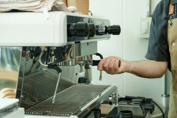 Adult male barista fitting portafilter on espresso machine inside cafe, demonstrating artisan skill, precision, and dedication, reflecting warmth of small family coffee business, small business
