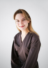 Portrait of a smiling young woman in a brown uniform, possibly a doctor or cosmetologist, looking at the camera on a light background.