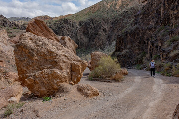 A hiker walks along a dirt road surrounded by massive boulders and rugged cliffs in the scenic...