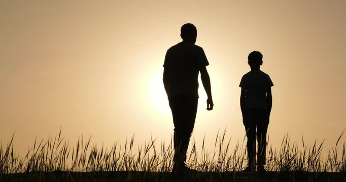 Silhouette man walking towards his son. Silhouette child son standing on hill and watching sunset. Father go his son and hugs him expressing support. Concept father day and support childr