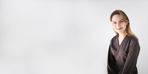 Banner portrait of a smiling female doctor in a brown medical uniform, sitting against a light background with copy space.