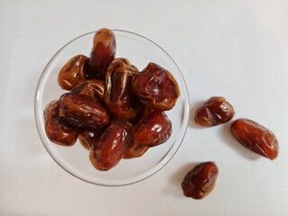 Dates in a glass bowl falling on a white background.