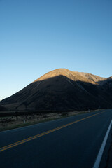 A straight road leads towards a majestic mountain illuminated by morning sun, creating a strong...