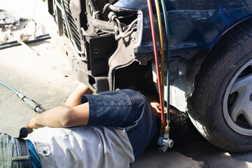 Automotive technician lying underneath a car, working on the air conditioning system using manifold...