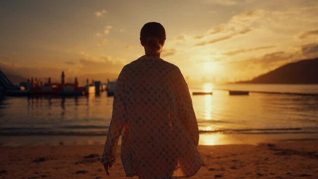 Traveling alone to ocean, back view of adult lady walking on sandy beach. Following shot, woman admiring sunset or sunrise and putting hands up, slow motion rear view shot, fascinating cloudscape