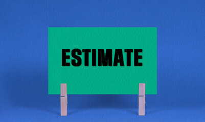 ESTIMATE Symbol. Concept words ESTIMATE on Green Rectangle Paper Held by Wooden Clothespin Blue...