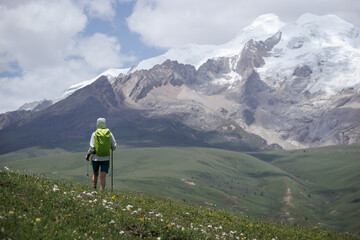 Naklejka premium Backpacking woman hiking on grassland kneeling down show respect to the holy snow capped mountains