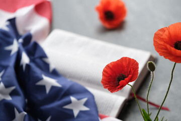 Bright poppy flowers nearby American flag partially on a grey background, a open bible. Remembrance day, Veterans day or Memorial day tribute on a grey background.