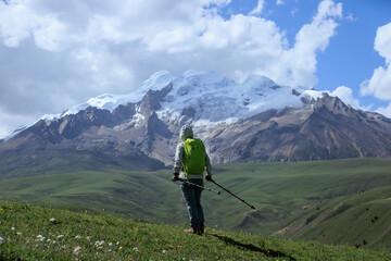 Obraz premium Backpacking woman hiking on grassland and snow capped mountains