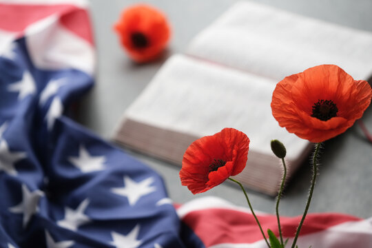 Bright poppy flowers nearby American flag partially on a grey background, a open bible. Remembrance day, Veterans day or Memorial day tribute on a grey background.