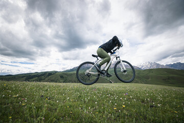 Woman cyclist riding mountain bike on grassland mountains with snow capped mountain in the distance