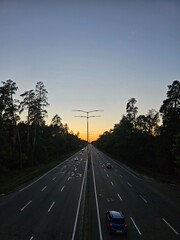 Cars driving on highway at sunset with forest and street light