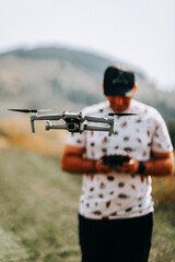Drone flying above a man controlling it in a grassy field during a sunny day