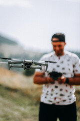 Drone flying over a man operating a remote controller in a natural landscape during daylight
