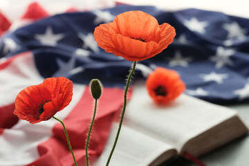 American flag decorated bright poppy flowers on a open Bible on a grey background. Remembrance day,...
