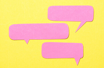 Pink blank cut out paper speech bubbles with copy space for text on yellow background, flat lay top view conceptual conversation backdrop