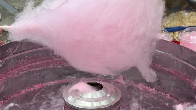 A close-up view of pink cotton candy being spun inside a metal cotton candy machine during preparation