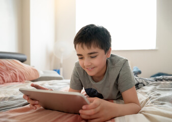 Young boy lying in bed using tablet computer at home,Kid leisure in casual digital lifestyle,...