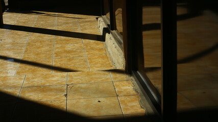 Sunlight streams into a minimalist interior, casting dramatic shadows on the tiled floor and dark wall panels. Creates a play of light and shade, highlighting textures and architectural lines