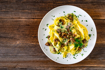 Papperdelle pasta with champignons mushrooms in cream sauce and parsley on wooden table