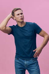Confused young man with short hair wearing casual blue t-shirt and jeans stands against pink...