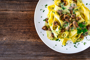 Papperdelle pasta with champignons mushrooms in cream sauce and parsley on wooden table