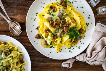 Papperdelle pasta with champignons mushrooms in cream sauce and parsley on wooden table