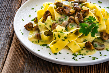 Papperdelle pasta with champignons mushrooms in cream sauce and parsley on wooden table