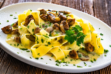 Papperdelle pasta with champignons mushrooms in cream sauce and parsley on wooden table