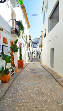 Fototapeta Narrow cobblestone street in a picturesque Spanish village. Whitewashed buildings line the street, adorned with colorful flowers and greenery.