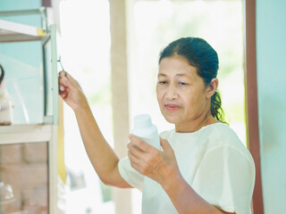 Senior Asian woman holding drugs for concept health care and medical. Healthy lifestyle people medicine bottle with pill for home care wellness health. Elderly care patient. Female reading drug labels