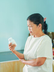 Senior Asian woman holding drugs for concept health care and medical. Healthy lifestyle people medicine bottle with pill for home care wellness health. Elderly care patient. Female reading drug labels
