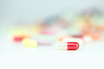 Red and white medical capsule on blurred background of colorful pills, symbolizing health,...