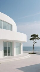 Modern white building with large windows overlooking the sea, accompanied by a solitary tree.