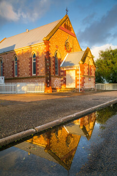An historic brick church reflected in roadside puddles