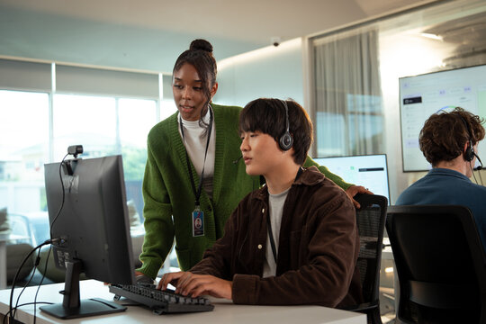 Professional team working in modern tech customer support office, with woman assisting colleague at computer. environment is collaborative and focused