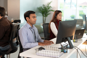 Focused team of tech customer support professionals working in modern office environment, using computers and headsets to assist clients efficiently