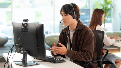 Focused tech support representative wearing headset is assisting customer at modern office desk,...